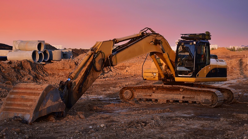 Excavator machine with sewage pipes in background