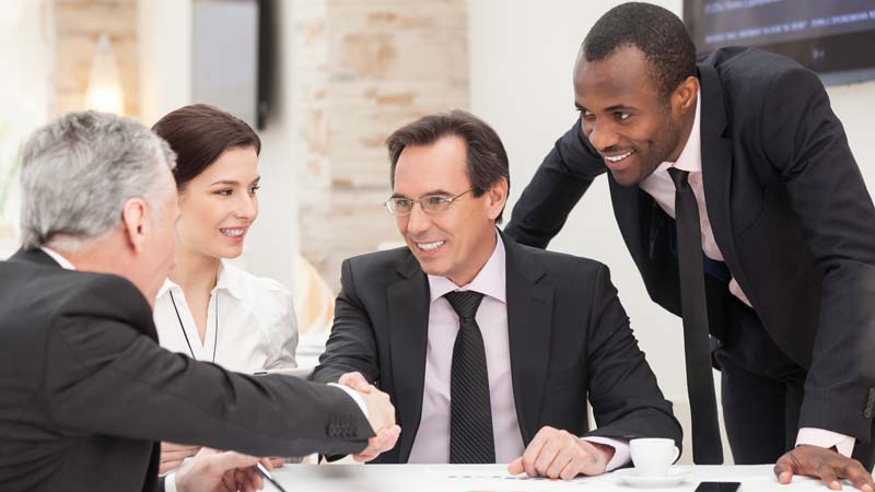 Four multiracial executives talking with two shaking hands