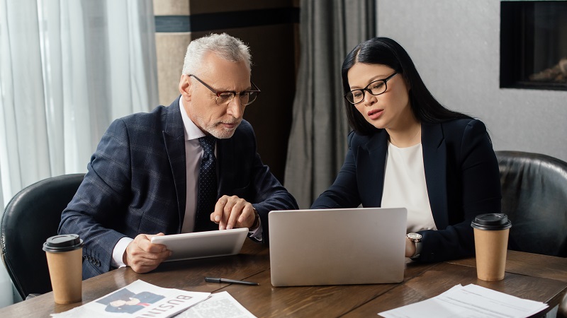 Two executives discussing project and reviewing data on a laptop and tablet